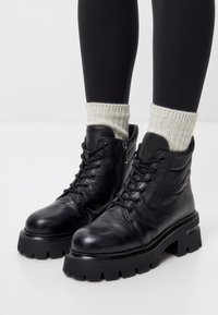 Zwarte leren enkellaarsjes met een chunky zool, vetersluiting, zijrits en geribbelde witte sokken, met een gladde textuur en robuuste constructie.