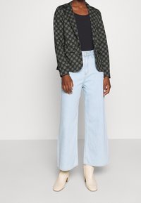 Černý blazer se zlatým vzorem, kombinovaný s světle modrými širokými džíny a smetanovými botami na blokovém podpatku. Pod tím jednoduché černé tričko.