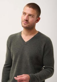 Donkergroene, geribbelde wollen trui met een V-hals en lange mouwen. Beschikt over een getailleerde silhouet en een gestructureerde stof.