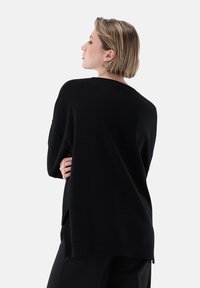 Schwarzer Strickpullover mit lockerer Passform, weitem Ausschnitt und überschnittenen Schultern. Weiche Textur mit Seitenschlitzen am Saum.