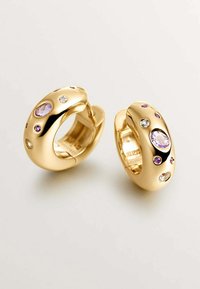 Pendientes de aro dorados con piedras preciosas de colores variados, incluyendo acentos morados y transparentes, con una superficie lisa y pulida y forma ovalada.