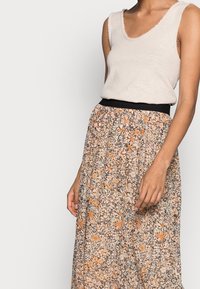 Bloemige maxi-rok in beige en oranje tinten met een zwarte elastische tailleband; gecombineerd met een lichtgekleurde mouwloze top.