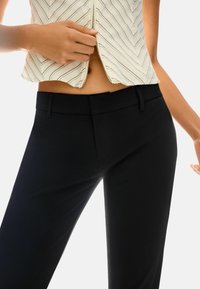 Schwarze maßgeschneiderte Hose mit glatter Textur, ausgestattet mit einem flachen Bund und dezenten Seitentaschen, kombiniert mit einem Oberteil im Zickzackmuster.