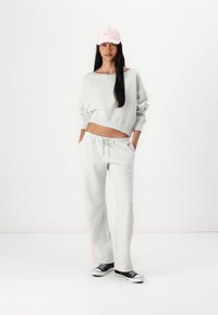 Sweatshirt court gris clair, pantalon assorti, tous deux en matériau doux. Baskets noires et casquette de baseball rose avec un détail textuel.