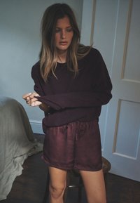 Bordowy dzianinowy sweter w połączeniu z pasującymi satynowymi szortami, wyposażonymi w elastyczny pas i sznurek do regulacji. Gładka faktura, luźny krój.