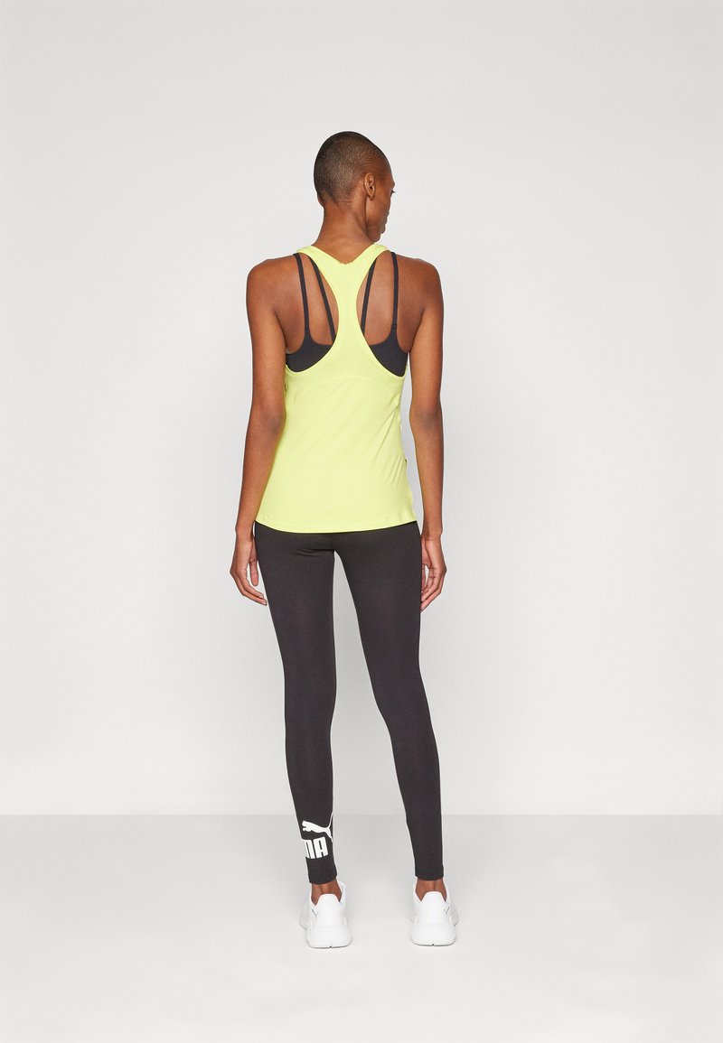 Canottiera sportiva verde lime con spalline nere, abbinata a leggings neri con un logo bianco, completata da scarpe da ginnastica bianche.