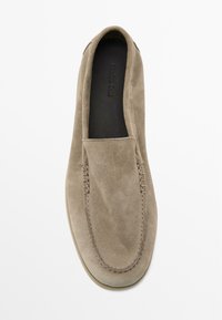 Scarpa slip-on in suede beige con punta arrotondata, dettagli cuciti lungo la tomaia e soletta nera liscia.