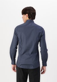 Navy blue long-sleeve shirt with a geometric pattern, button cuffs, and a structured collar. Smooth fabric with a slight sheen.