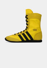 Yellow high-top sneaker with black laces and three black stripes. Features a suede and synthetic upper with a rubber sole.