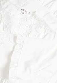 Bílá blůza s propracovanými výšivkami, řasenými manžetami a texturou z nahrnuté látky. Štítek uvádí "Missguided," velikost UK 8.
