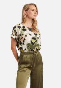 Korte mouwen top in roomkleur met groen en zwart dierenprint; gecombineerd met olijfgroene satijnen broek met trekkoord in de taille. Gladde textuur.