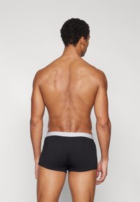 Schwarze Boxer-Briefs mit einem grauen elastischen Bund, die eine glatte Stofftextur und ein enganliegendes Design aufweisen, von hinten gezeigt.