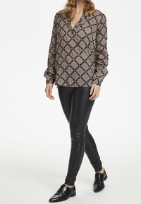 Blusa a maniche lunghe in tessuto a fantasia con scollatura a V, abbinata a leggings in pelle nera attillati e scarpe eleganti nere.