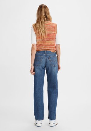 Pletený oranžový a červený pruhovaný bezramínkový top spárovaný s modrými džínami s vysokým pasem. Bílé tenisky doplňují tento outfit.