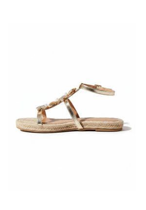 Flad sandal med gyldne metalstropper, ankelspænde, dekoreret med perler og skaller, og en vævet beige sål.