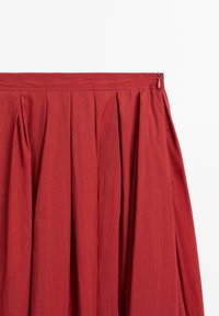 Punainen drapé-hame, jossa on teksturoitu pinta, sivuvetoketju ja kerätty vyötärö. Hame on suunniteltu virtaavaksi A-linjaiseksi siluetiksi.