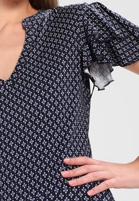 Námořnická blůza s květinovým vzorem, volány na průhledných rukávech, výstřihem do V a přiléhavým korpusem. Měkká textilie a ženské detaily.