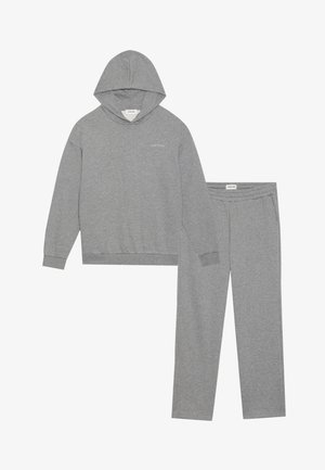 Šedá bavlněná souprava sweatpantů a mikiny. Mikina má klokaní kapsu a ribovaná manžety; kalhoty mají elastický pas a postranní kapsy.