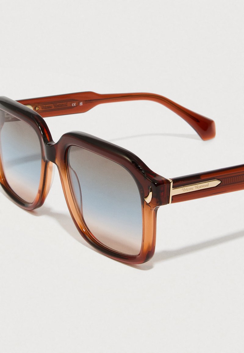 Lunettes de soleil écaille de tortue marron avec une monture carrée, des verres dégradés, des accents dorés et un logo sur les branches.