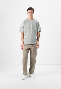 Grey short-sleeve t-shirt with a relaxed fit, paired with light brown pants and white sneakers. Smooth fabric and minimal design.