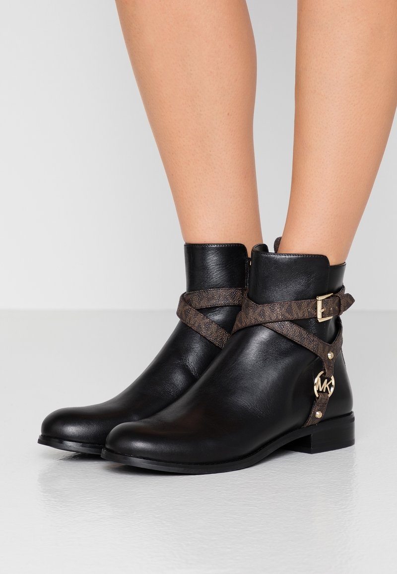Bottines en cuir noir avec une sangle à motif marron et des garnitures dorées, dotées d'un petit talon carré et d'une fermeture éclair.