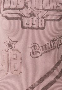 Rosa ribbad linne med grafiska tryck i mörkgrått, inklusive "1998" och stjärnmotiv, med texturerad yta och en smal passform.