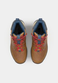 Bottes de randonnée en cuir marron avec des lacets rouges, un col rembourré gris et des accents bleus. Présente des œillets en métal et une semelle en caoutchouc texturé.