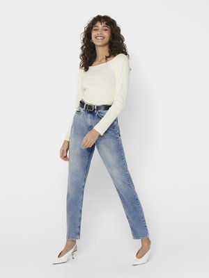 Lys gul langærmet top med firkantet halsudskæring, parret med blå højtaljede jeans og hvide hæle. Casual, tætsiddende design.