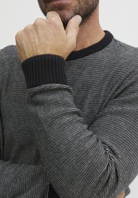 Suéter a rayas blanco y negro con puños y cuello negro acanalados, que presenta un diseño de tejido texturizado y mangas ajustadas.