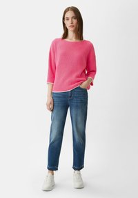 Rosa gerippter Strickpullover mit Dreiviertelärmlen, kombiniert mit hellblauen, geraden Jeans und weißen Turnschuhen.