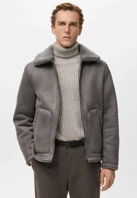 Grijze buitenkleding met een zachte kraag, gemaakt van een glad materiaal, met twee zijzakken en een ritssluiting, gedragen over een lichte trui.