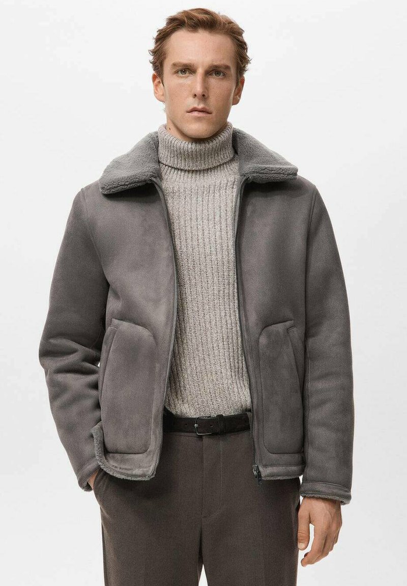 Grijze buitenkleding met een zachte kraag, gemaakt van een glad materiaal, met twee zijzakken en een ritssluiting, gedragen over een lichte trui.