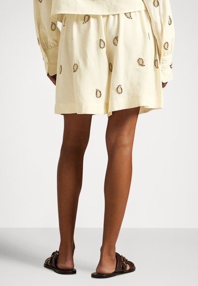Lysegule shorts lavet af bomuld med en afslappet pasform, der har broderede ovale former i guld. Kombineret med brune sandaler.