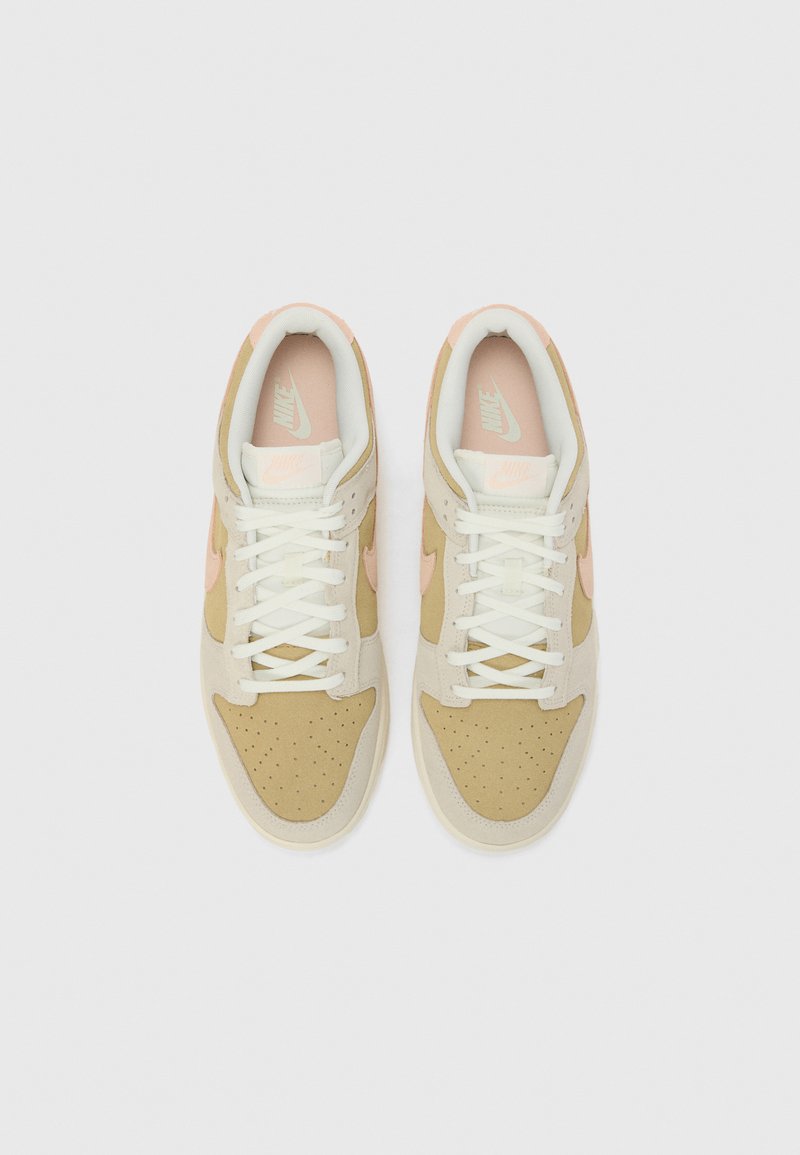 Sneakers Nike z górną częścią z brązowej i beżowej zamszowej skóry, białymi sznurówkami, różowymi akcentami na logo Swoosh i pięcie oraz perforowanym noskiem.