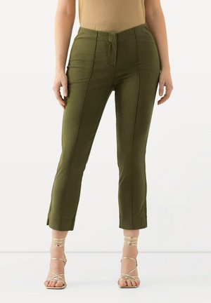 Pantaloni aderenti verde oliva con una texture liscia, di lunghezza cropped e dettagli con spacchi laterali. Presentano pieghe frontali e vita a media altezza.