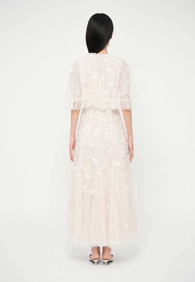 Μακρύ, διάφανο, ανοιχτό μπεζ φόρεμα με κεντήματα με λουλούδια, κοντά μανίκια με βολάν και ρέουσα σιλουέτα. Η πλάτη διαθέτει απλό κούμπωμα.