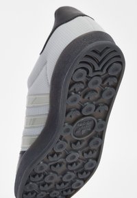 Šedá podrážka bot Adidas s kruhovými vzory vzorku a logem Adidas uprostřed, nakloněná na jednoduchém bílém pozadí.