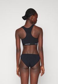 Soutien-gorge de sport noir avec un design dos nageur et une inscription blanche "PIECES". Culotte hipster noire assortie, les deux en tissu doux et extensible.