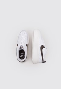 Zapatillas deportivas blancas con puntera perforada, swoosh de cuero marrón, acolchado en el collar y suela de goma texturizada. Cierre con cordones para un mejor ajuste.