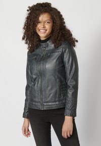 Giacca da motociclista in pelle nera con design aderente, chiusura con zip frontale, due tasche sul petto e dettagli a coste sulle maniche.