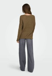 Maglione lavorato a maglia marrone con scollo ampio e spalle cadenti, abbinato a pantaloni in denim grigi dal taglio morbido.