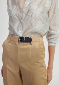 Blusa transparente a rayas con bordado en forma de nube en blanco, combinada con pantalones beige ajustados. Cinturón de cuero negro con hebilla de plata.