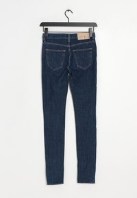 Tmavě modré skinny džíny s hladkou denimovou strukturou, pěti kapsami a prošitými detaily. Zavěšené na černém kovovém háčku.