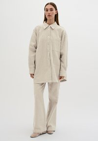 Hellbeige strukturierte oversized Knopfleiste-Hemd mit Kragen, kombiniert mit passenden Schlaghosen. Verfügt über ein gestricktes Muster und eine einzelne Brusttasche.