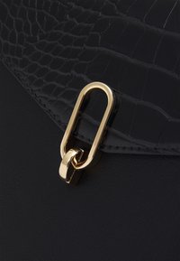 Sac à main noir avec un motif de crocodile texturé, finition lisse et quincaillerie dorée. La fermeture est dotée d'un grand lien ovale.