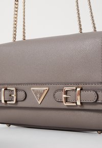 Grå læder håndtaske med tekstureret overflade, guldfarvede detaljer, et trekantet logo og dobbelte spænder på forsiden.