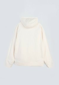 Jasno beżowy, gładki dres z kapturem i długimi rękawami, w luźnym kroju, pokazany z tyłu na jasnym tle.