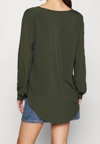 Chemise à manches longues vert olive avec un décolleté en scoop et des détails froncés aux épaules, assortie à un short en denim avec un ourlet effiloché.