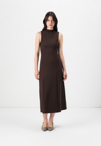 Brun ärmlös midiklänning med hög hals och åtsittande liv. Slät textur, utsvängd kjol, matchad med nude klackskor med spetsig tå.