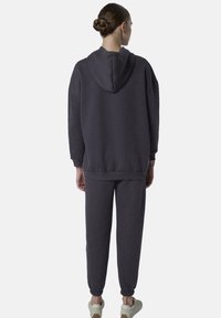 Donkergrijze sweater met capuchon, met een losse pasvorm, elastische manchetten en bijpassende joggingbroek met taps toelopende enkels. Glad textuur.